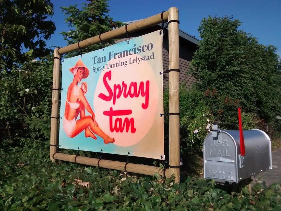 Het bord van Tan Francisco Spray Tanning Lelystad, met een pin-up in zonnehoed en de woorden Spray tan, tussen twee houten palen